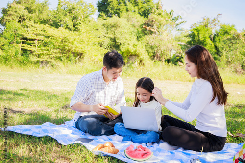 Happy family picnic. Asian parents, little girl playing laptop and have fun together during picnic