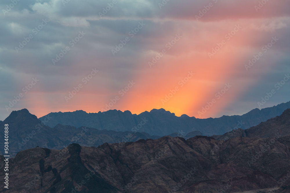 Dramatic scenes with red rays of the sun, cloudy sky and dark silhouette of Sinai mountains. Dahab, Sinai peninsula, Egypt
