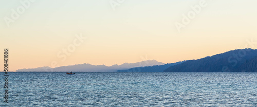 Boat in the Red Sea on the horizon on the background of a beautiful sunset with orange sky in Lagoona beach. Dahab, Egypt