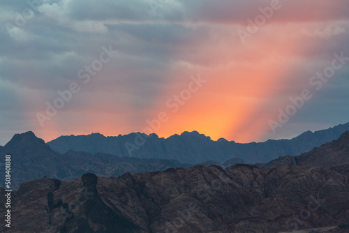 Dramatic scenes with red rays of the sun, cloudy sky and dark silhouette of Sinai mountains. Dahab, Sinai peninsula, Egypt