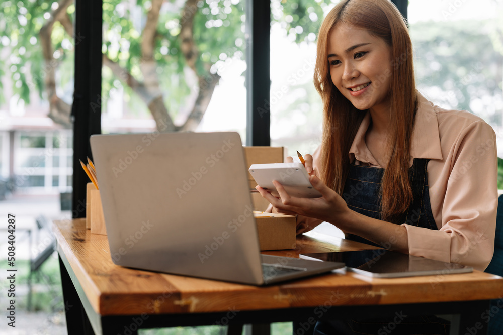 Asian woman entrepreneur using calculator with pencil in her hand, calculating financial expense at home office,online market packing box delivery,Startup successful small business owner,SME, concept Asian woman entrepreneur using calculator with pencil in her hand, calculating financial expense at home office,online market packing box delivery,Startup successful small business owner,SME, concept