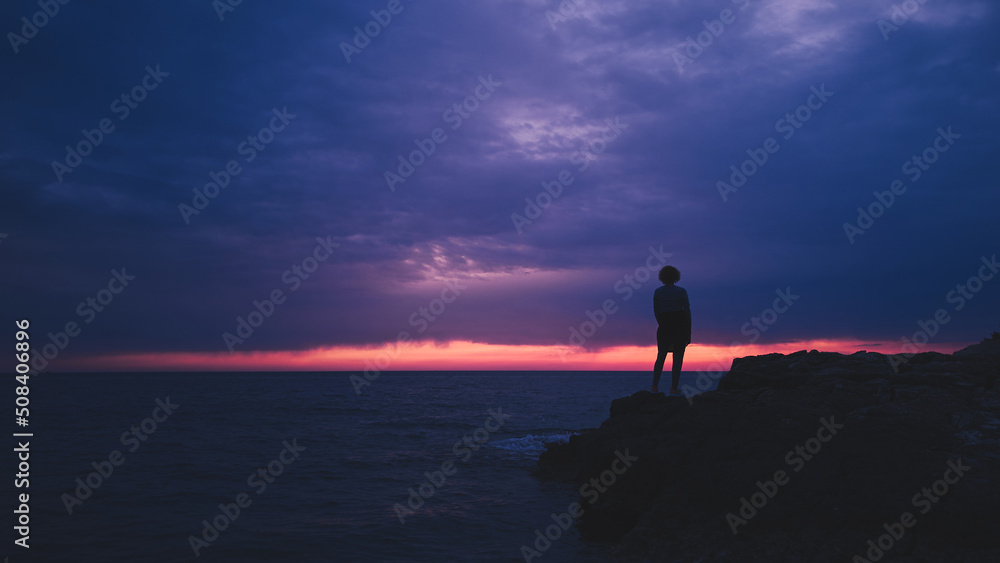 Silhouette of a woman watching sunset over distant horizon.