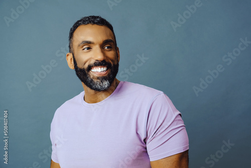 headshot of a handsome smiling african american man with beard and mustache purple shirt on a gray background looking away at copy space studio