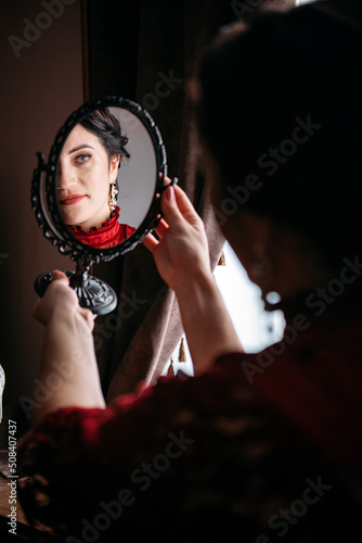 Portrait of beautiful woman in red vintage 1800s early 1900s clothing with mirror. photo
