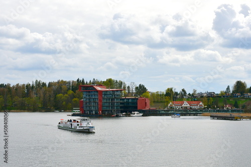 A view of a luxirious boat parked next to a small wooden marina, pier or platform with a metal ladder for entering and exiting the vessel seen next to a lush forest or moor on a cloudy spring day photo