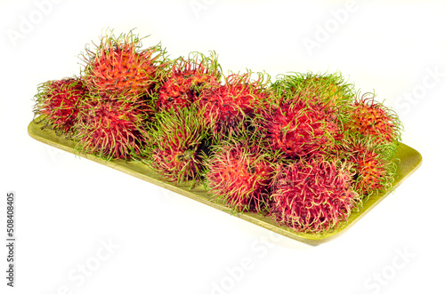 Red and yellow rambutan on wooden plate on a white background