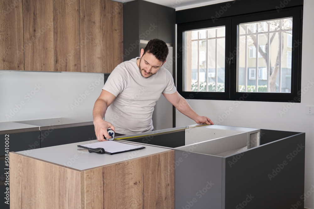 Young hispanic man using measuring tape before placing countertops on modern kitchen.