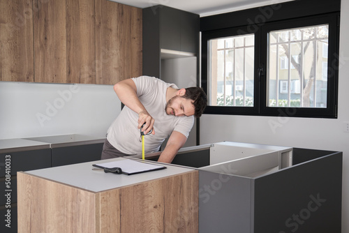 Young hispanic man using measuring tape before placing countertops on modern kitchen. photo