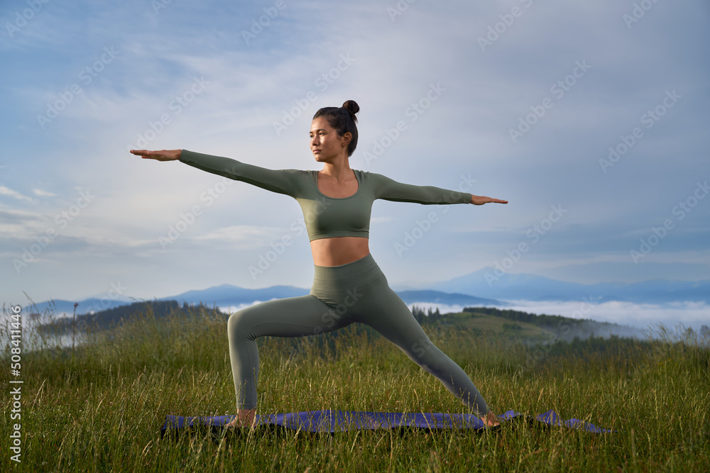 Sporty woman in activewear doing yoga exercises among summer mountains. Healthy fit lady with dark hair spending free time for outdoors workout. Sporty woman in activewear doing yoga exercises among summer mountains. Healthy fit lady with dark hair spending free time for outdoors workout.
