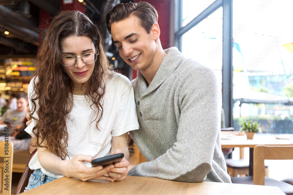 Título: Smiling couple at cafe using mobile phone Título: Smiling couple at cafe using mobile phone