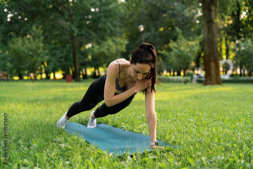 a girl outdoors in the park goes in for sports in a sports purple top in black leggings on a blue sports mat in the background a meadow and trees