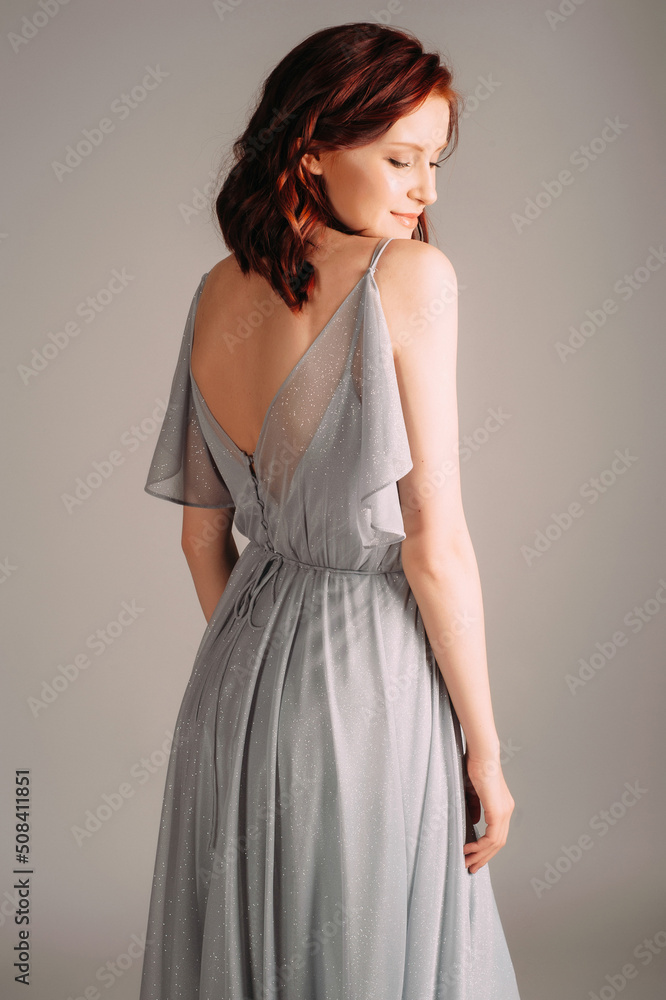 Beautiful young woman in dust blue dress. Studio portrait of ginger lady in evening gown dancing on high heel shoes in studio. Bridesmaid's outfit for hen party, rear view. Beautiful young woman in dust blue dress. Studio portrait of ginger lady in evening gown dancing on high heel shoes in studio. Bridesmaid's outfit for hen party, rear view.