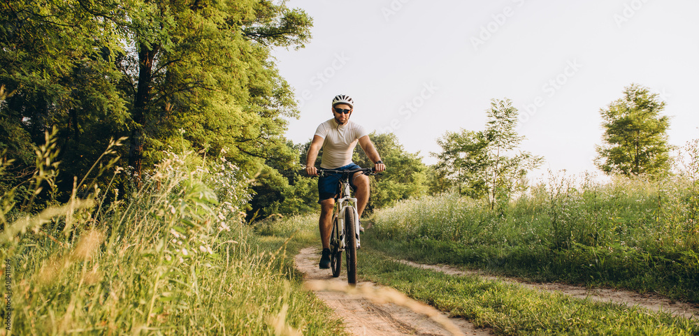A man rides a bicycle on a dirt road in the summer at sunset. Active rest in the summer on bicycles.