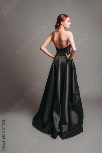 Black ball gown. Attractive ginger young woman in sleeveless evening dress on studio background. Holiday outfit. A line backless dress. Dramatic look. photo