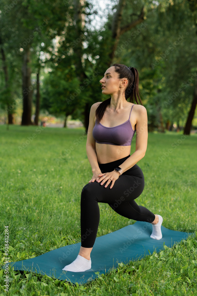 a girl outdoors in the park goes in for sports in a sports purple top in black leggings on a blue sports mat in the background a meadow and trees
