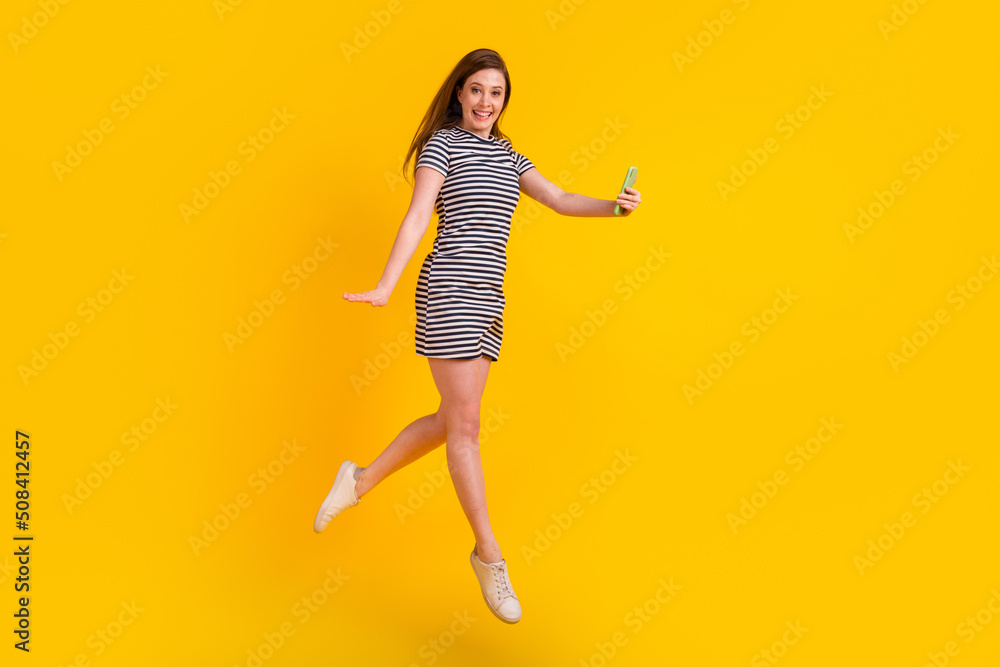 Full length profile side photo of young girl jump make selfie cellphone trip isolated over yellow color background Full length profile side photo of young girl jump make selfie cellphone trip isolated over yellow color background