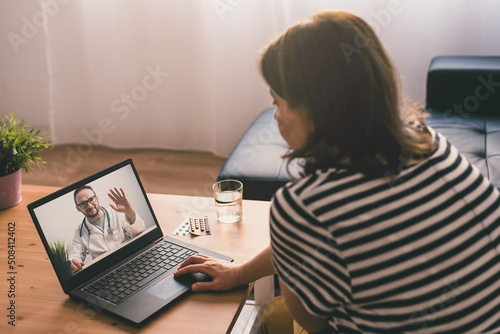 Fotografie Woman sitting on a sofa and talking with a doctor online using laptop