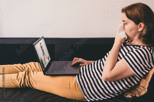 Woman lying on a sofa and talking with a doctor online using laptop. Telemedicine concept.
