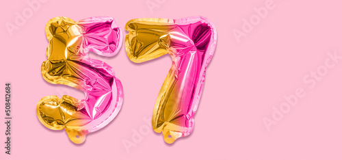 Rainbow foil balloon number, digit fifty seven on a pink background. Birthday greeting card with inscription 57. Top view. Numerical digit. Celebration event, template. Banner
