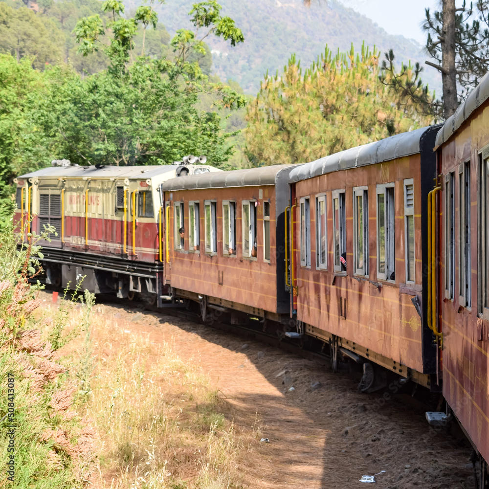 Obraz premium Toy Train moving on mountain slopes, beautiful view, one side mountain, one side valley moving on railway to the hill, among green natural forest. Toy train from Kalka to Shimla in India