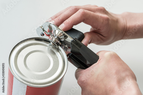 Photos Hands opening a can in a kitchen with a tin opener.
