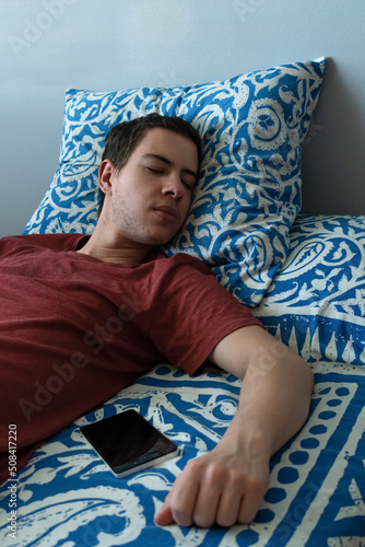 Millennial sleeping in bed near his mobile phone