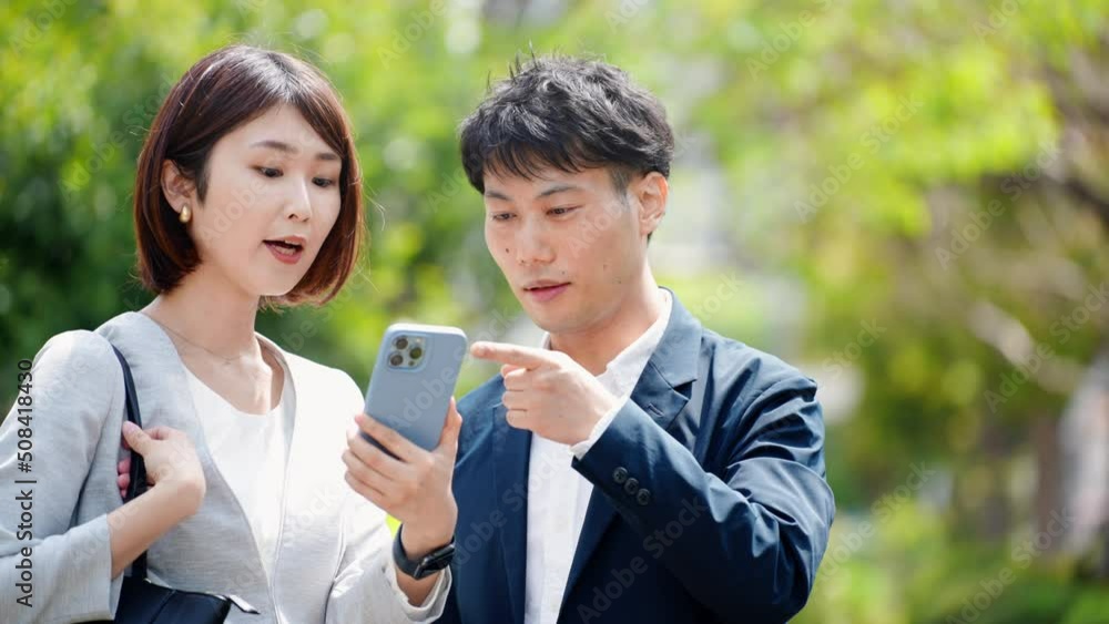 屋外がスマートフォンを操作しているビジネスウーマンとビジネスマン