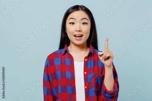 Young insighted smart proactive woman of Asian ethnicity 20s in checkered shirt hold index finger up with great new idea isolated on plain pastel light blue color background. People lifestyle concept.