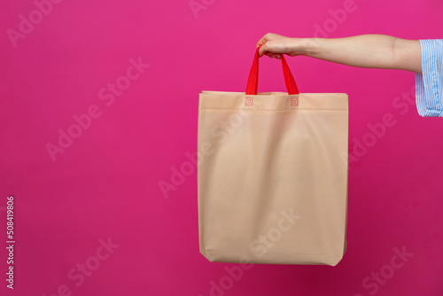 Female hand holding eco or reusable shopping bag against pink background