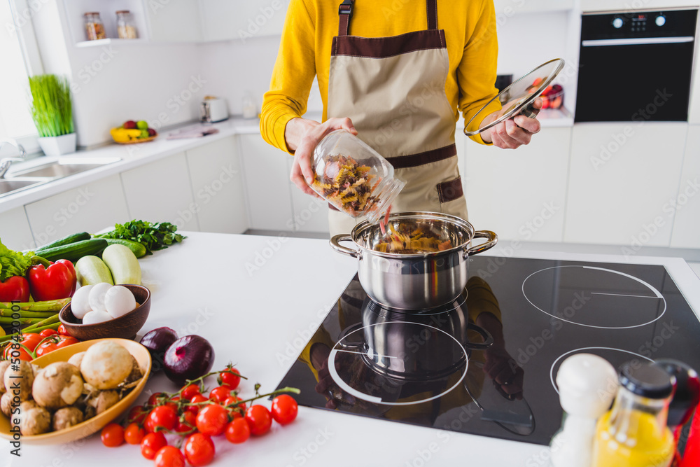 Cropped close up photo of young guy add pasta boil prepare kitchen cuisine healthy dish calories indoors Cropped close up photo of young guy add pasta boil prepare kitchen cuisine healthy dish calories indoors