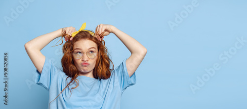 Fotografie, Tablou Emotional young redhead girl, student having fun isolated on blue studio background