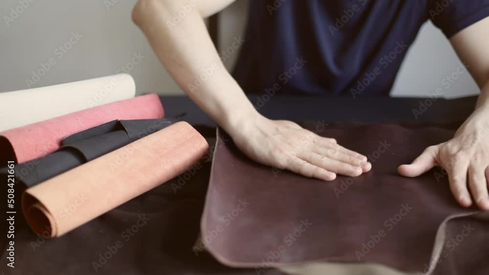 A professional craftsman, sitting at his desk and choosing cowhide in a roll for making leather products A professional craftsman, sitting at his desk and choosing cowhide in a roll for making leather products