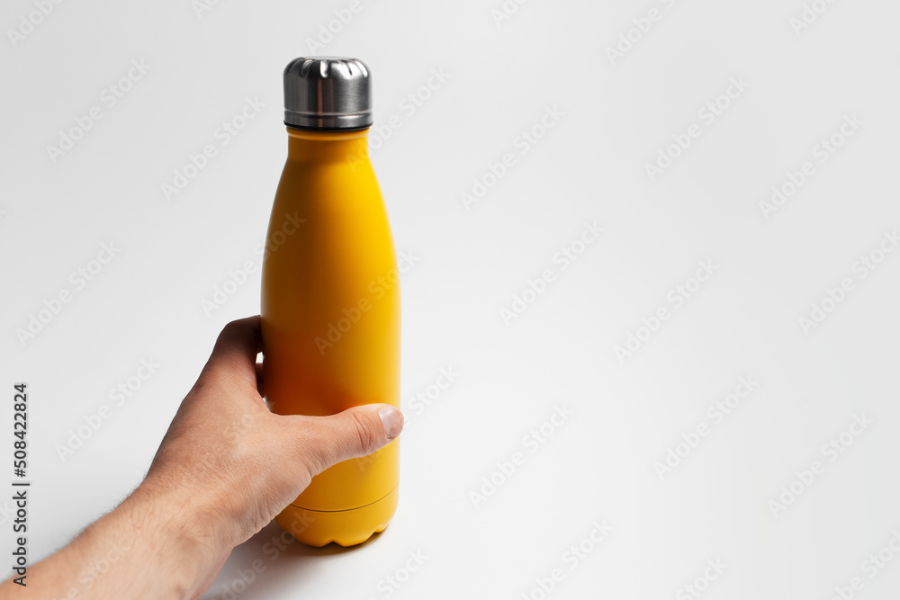 Close-up of male hand holding steel eco reusable water bottle of yellow on white. Close-up of male hand holding steel eco reusable water bottle of yellow on white.