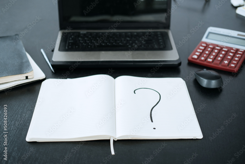 Question mark in a notepad on the background of a laptop and a calculator Question mark in a notepad on the background of a laptop and a calculator