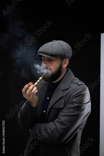 Bearded stylish man smoking a pipe man smokes a pipe on a dark background