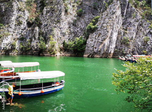 Journey to the Matka canyon in Macedonia. Emerald water in the lake, many tourist boats against the backdrop of high rocks and mountains. A man enters the water on the steps 