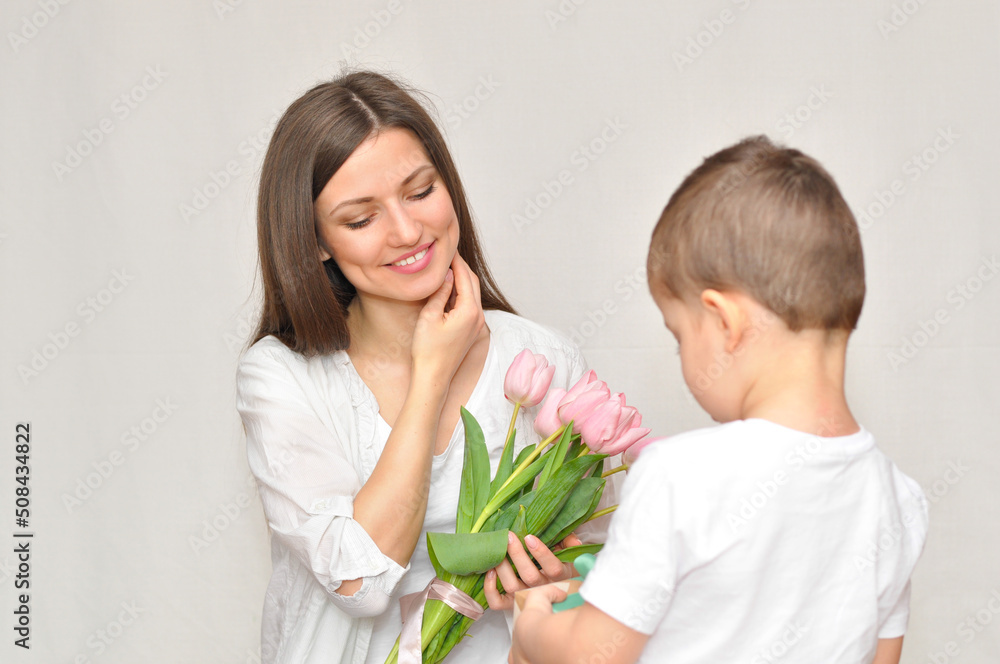 Little child son gives his mother a bouquet of delicate pink tulips. Mother's Day celebration. Little child son gives his mother a bouquet of delicate pink tulips. Mother's Day celebration.
