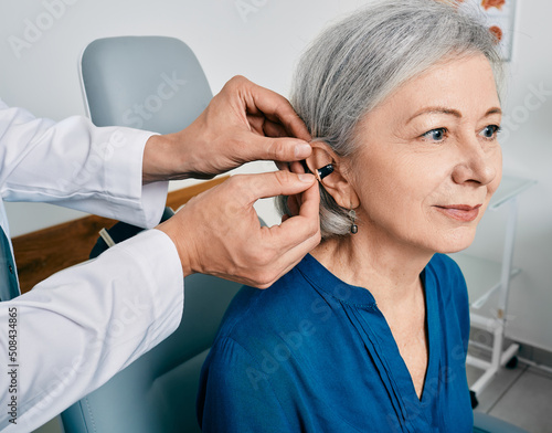 Senior woman during installation hearing aid into her ear by her audiologist  close-up. Hearing treatment for hearing impaired people
