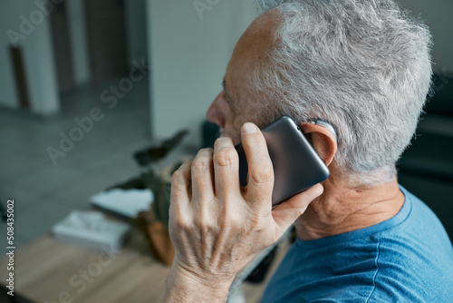 Elderly man with hearing aid has a full life and can hear interlocutor on phone. Hearing solution and innovation technology photo
