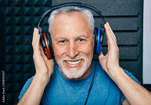 Hearing loss treatment. Positive senior man wearing audiometry headphones while hearing test and audiogram in special audio room photo