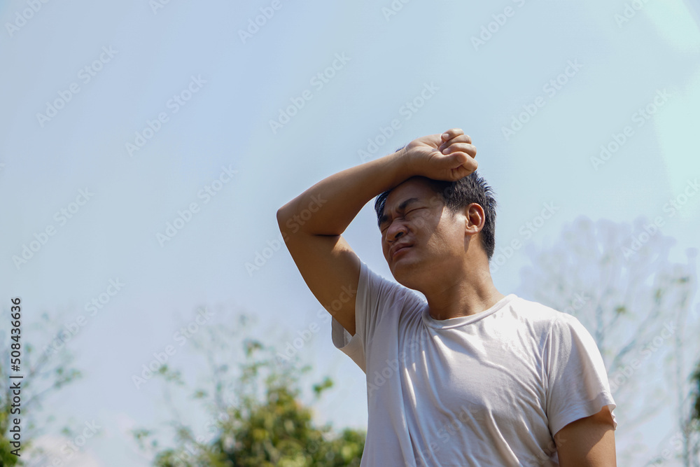 Asian middleaged man feels hot, stands outdoor in sunny day. Concept