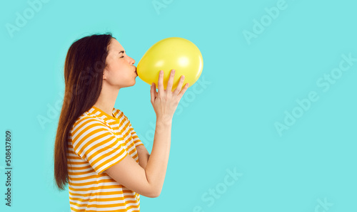 Quadro em tela Young woman preparing for party funny blowing yellow balloon isolated on light blue background