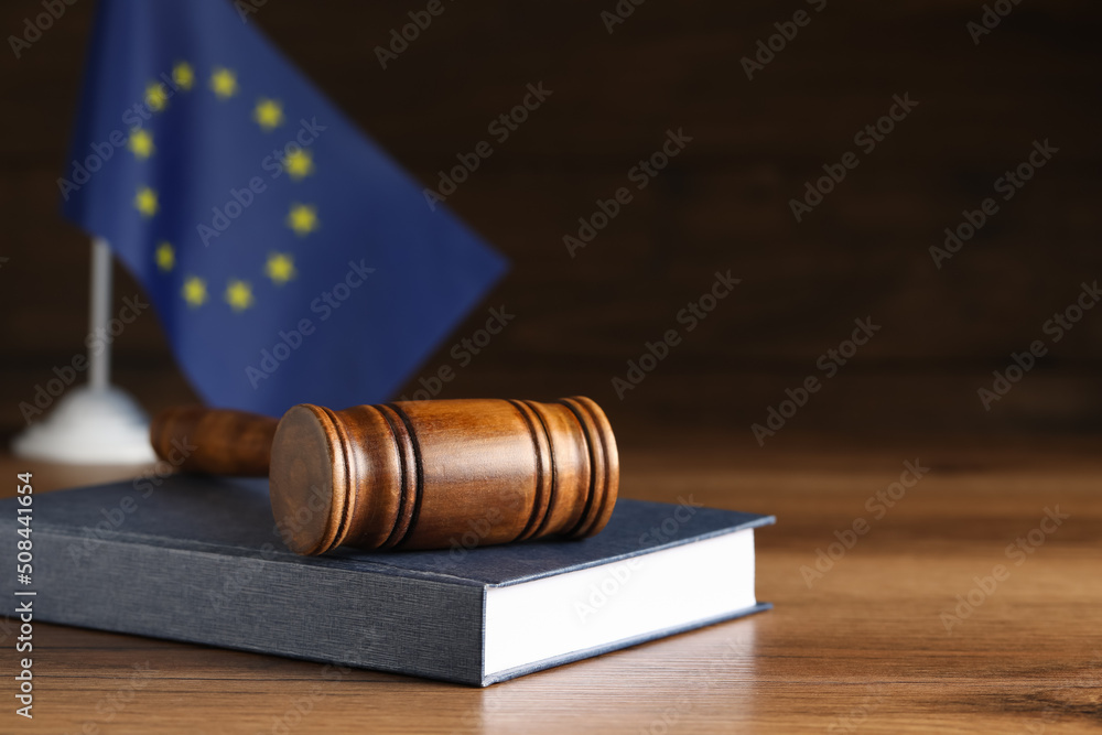 Judge's gavel and book on wooden table against European Union flag. Space for text