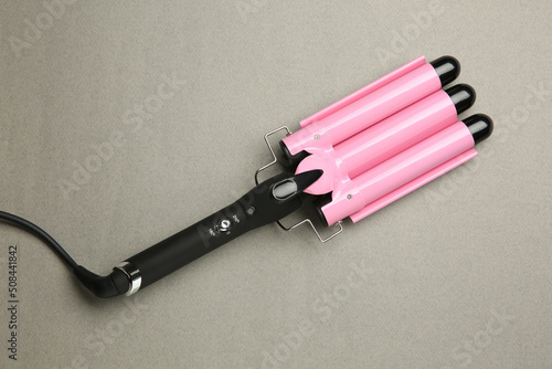 Modern triple curling hair iron on grey background, top view