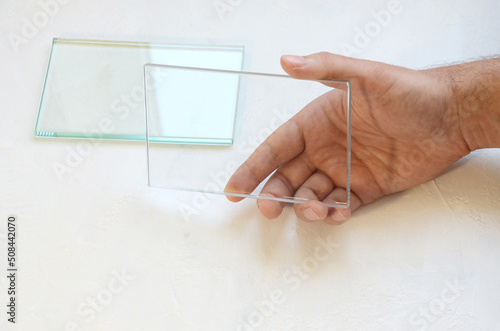 male hand holding glass sample, transparent glass in hand on white background, industrial glass