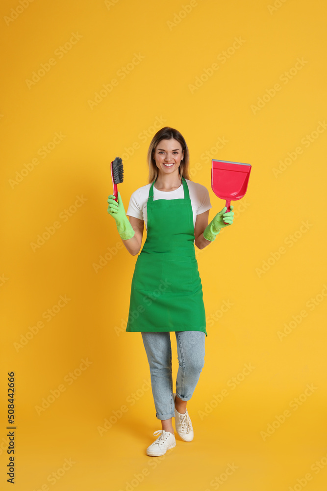 Young woman with broom and dustpan on orange background Young woman with broom and dustpan on orange background
