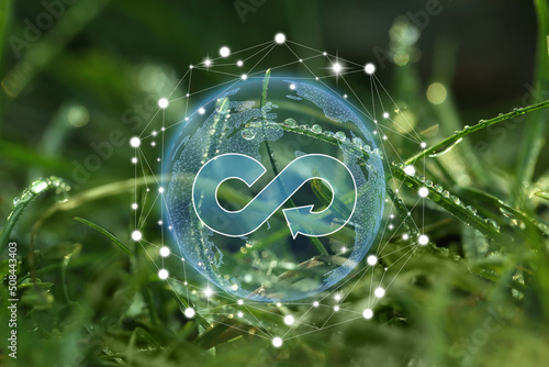 Circular economy concept. Green grass with dew and illustration of infinity symbol in Earth photo