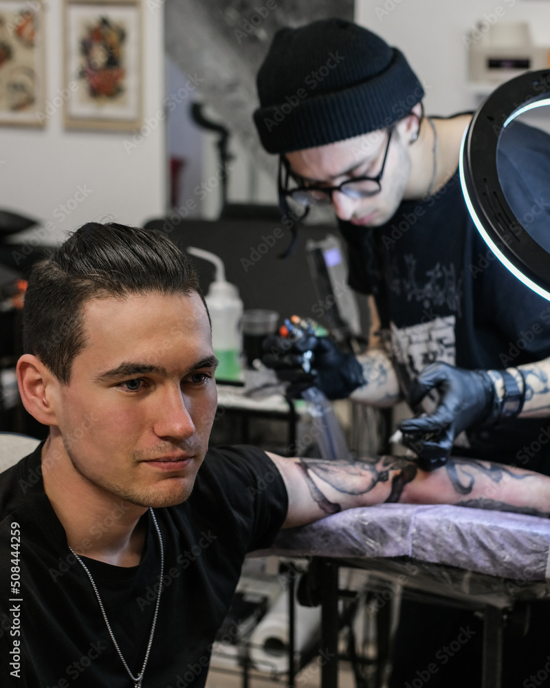 Professional tattoo artist stuffs a tattoo on the man's hand. Tattoo