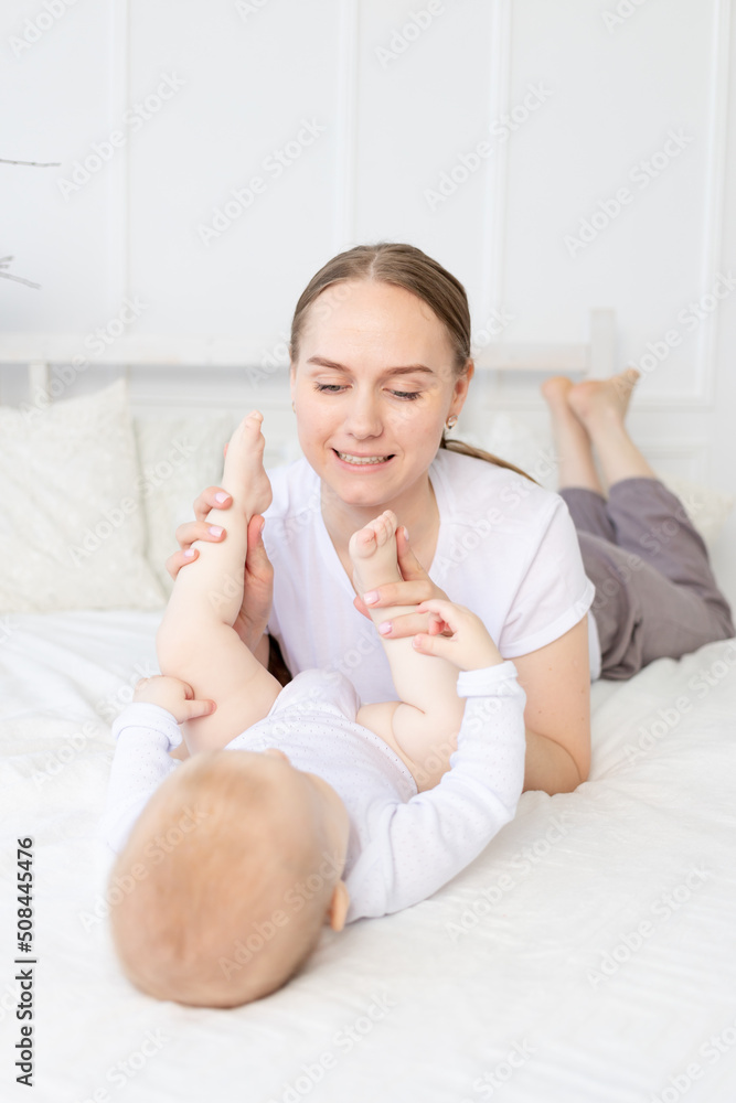 happy mother with baby playing with his legs on the bed at home happy mother with baby playing with his legs on the bed at home
