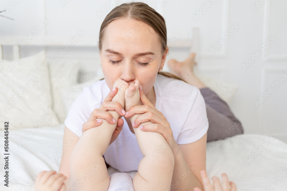 mother kisses baby's feet and sniffs them on the bed at home, happy motherhood mother kisses baby's feet and sniffs them on the bed at home, happy motherhood